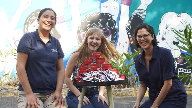 Student and two staff members smiling to the camera with a table filled with sustainable menstruation products